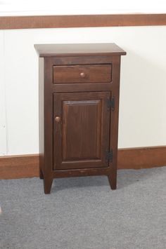 a small wooden cabinet sitting on top of a carpeted floor next to a wall