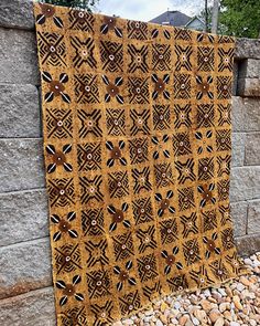 a yellow and black quilt sitting on top of a pile of rocks next to a stone wall