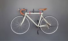 a white bicycle hanging on the side of a wall with a brown handlebars