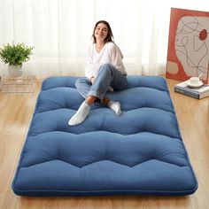 a woman sitting on top of a blue mattress in the middle of a wooden floor