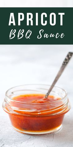 a glass jar filled with bbq sauce on top of a white tablecloth next to a spoon