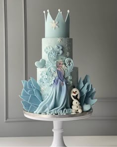 a three tiered cake with blue frosting and decorations on the top, sitting on a white pedestal