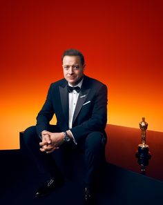 a man in a tuxedo is posing for a photo with an oscar statue behind him