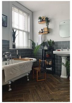 a bath tub sitting under a window next to a white sink and wooden flooring