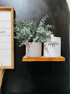 two potted plants sitting on top of a wooden shelf next to a framed sign