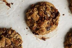 several chocolate chip cookies on top of a white paper covered countertop with crumbs