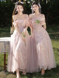 two women in pink dresses standing next to each other on a grass covered field with flowers