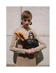 a woman holding a handbag and some bread in her other hand while standing next to a wall