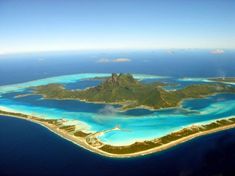 an island in the middle of the ocean with blue water and white sand on it