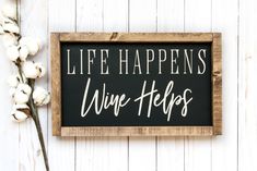 a sign that says life happens wine helps on it next to some cotton stalks and a plant