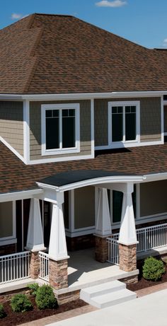 the front of a house with white pillars and brown shingles on it's roof