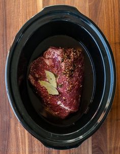 a piece of raw meat in a black crock pot on a wooden table top