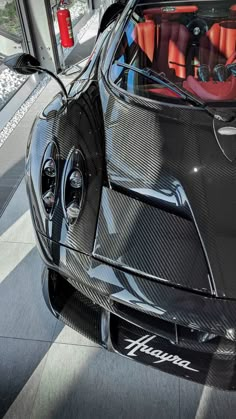 the front end of a black sports car with its hood up and red seats in it