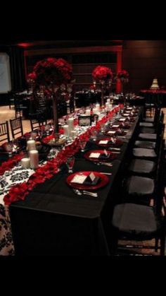 the table is set up with black and red flowers, candles, and place settings