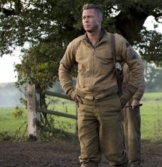 a man standing in front of a fence with his hands on his hips and looking at the camera