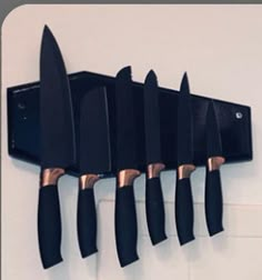 five knives are hanging on the wall with black handles and gold tips in front of them