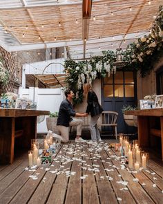 two people sitting at a table with candles in front of them and flowers on the floor