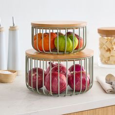 two metal baskets filled with onions and apples on top of a counter next to other kitchen utensils