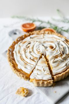 a pie with white frosting sitting on top of a table next to an orange slice