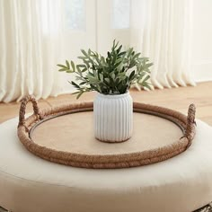 a white vase sitting on top of a round ottoman with a plant in the middle