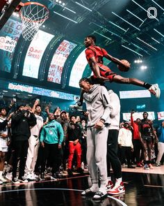 two young men standing on top of each other in front of a basketball hoop while people watch