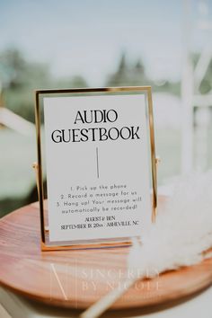 an audio guest book sitting on top of a wooden table next to a white feather