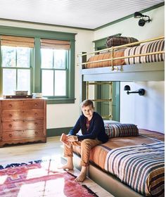 a young boy sitting on top of a bed in a room with bunk beds and dressers