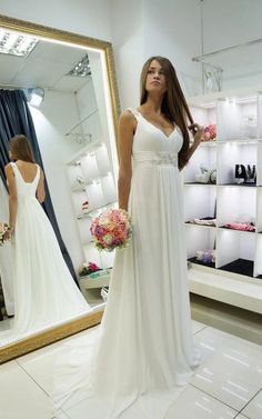 a woman standing in front of a mirror wearing a white dress