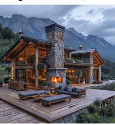 an outdoor living area with couches and fireplace in front of a mountain house at dusk