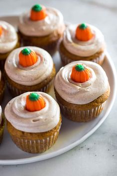 cupcakes with frosting and mini pumpkins on top sit on a plate