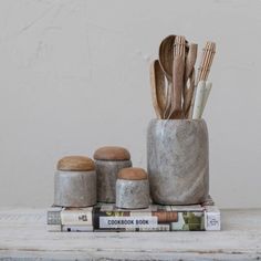 an assortment of kitchen utensils and wooden spoons in a stone container on top of books