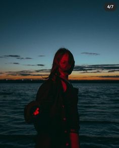 a woman standing in front of the ocean at night with her hands on her hips