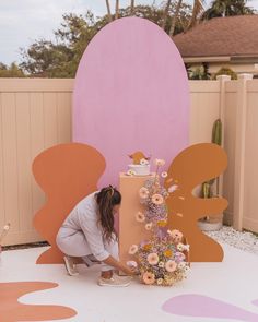 a woman kneeling down next to a tall cake on top of a white and pink floor