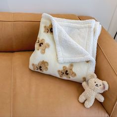 a teddy bear laying on top of a brown couch next to a white and black blanket