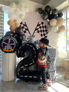 a young boy standing in front of a giant number six balloon sculpture with balloons around it