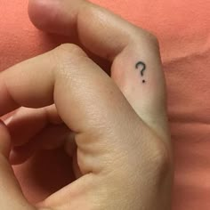 a person's hand with a small tattoo on their left index finger, which has a question mark in the middle