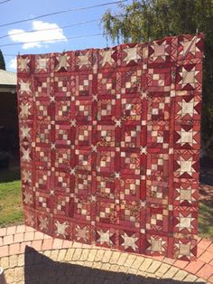 a red and white quilt is hanging on a brick wall in front of a house