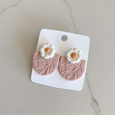 two pink and white flower earrings sitting on top of a card