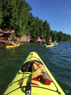 several people in kayaks paddling on the water near some cliffs and trees,