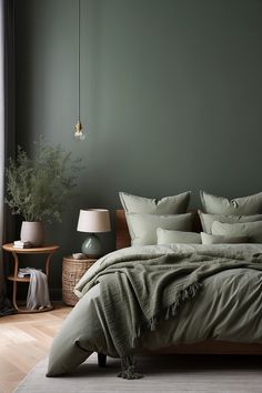 a bed with green sheets and pillows in a room next to a lamp on a table