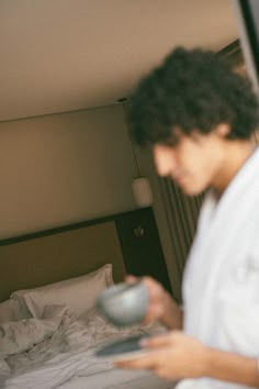 a young man holding a remote control in his hand while standing next to a bed