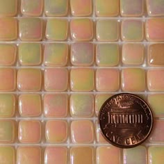 a penny sitting on top of a white tile floor with pink and purple tiles in the background