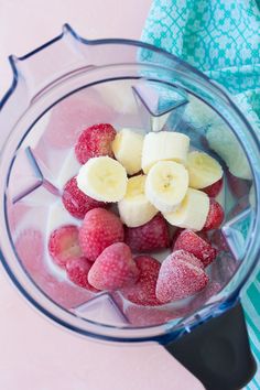 strawberries, bananas and other fruit in a blender on a pink tablecloth