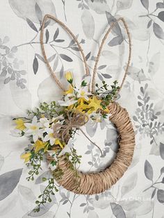 a wicker wreath with yellow and white flowers hanging from it's sides on a floral wallpaper