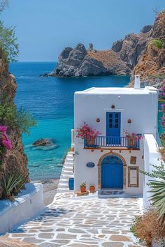 a white house with blue doors and flowers on the steps leading to the water's edge