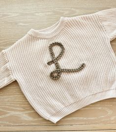 a knitted sweater with the letter q on it sitting on top of a wooden table