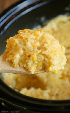 a wooden spoon full of food sitting in a crock pot with corn on top