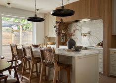 a kitchen with an island and wooden chairs in front of the counter top, along with large windows