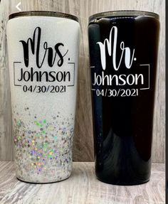 two personalized tumblers are sitting next to each other on a wooden surface, one is black and the other is white