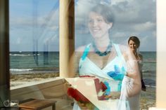 a woman standing in front of a window next to the ocean